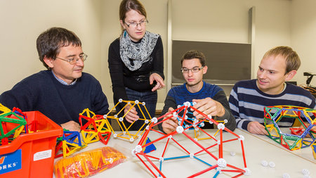 A professor speaks with students about polyhedrons on a table