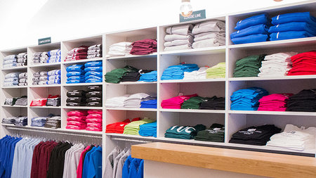 Verschiedenfarbige T-Shirts und Hoodies liegen in Regalen des Uni-Shops