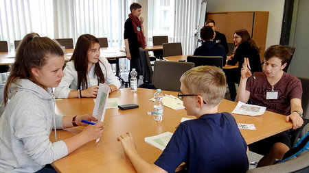 Schüler lösen gemeinsam eine Wettbewerbsaufgabe an einem Tisch.