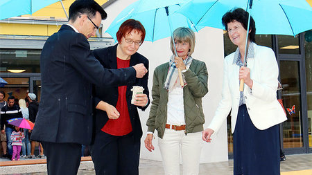Ein Mann und drei Frauen stehen mit Regenschirmen draußen.