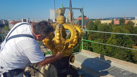 Mann streicht mit einem Pinsel an der Krone auf dem Böttcher-Bau der TU Chemnitz.