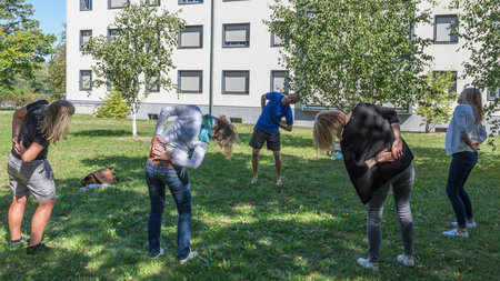 Vier Kursteilnehmerinnen machen unter Anleitung des Kursleiters Übungen im Freien.