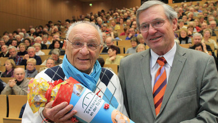 Dem mit 90 Jahren ältesten Teilnehmer des Seniorenkollegs wird eine Zuckertüte übergeben. 
