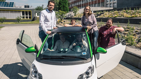 Forschende sitzen in einem bzw. stehen neben einem Elektromobil