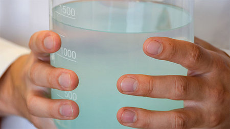 Zwei Hände umfassen ein mit Wasser gefülltes Messgefäß