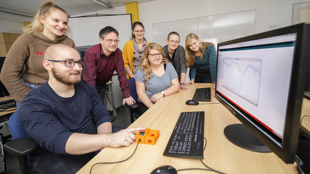 Studierende und Professor schauen auf einen Monitor