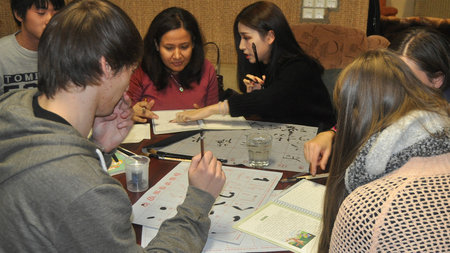 Mehrere Personen sitzen an einem Tisch und schreiben mit Tinte asiatische Schriftzeichen