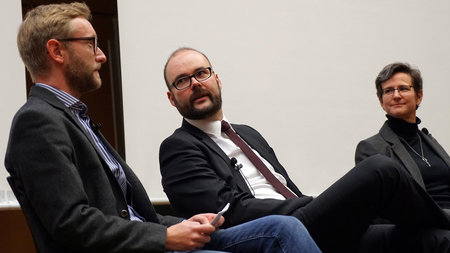 Zwei Männer und eine Frau sitzen im Podium.