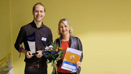 Ein junger Mann und eine junge Frau halten Blumen und Urkunde in den Händen.