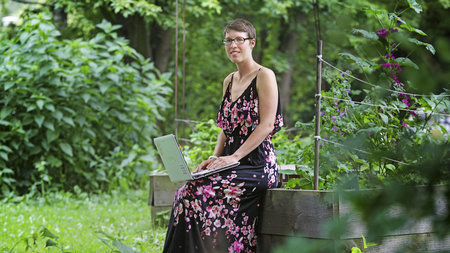 Frau steht im Garten und hält Laptop in der Hand