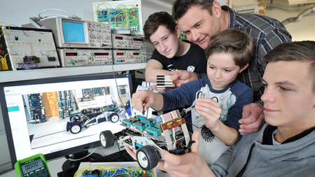 Mann experiementiert mit drei Kindern im Labor an einem Modellauto