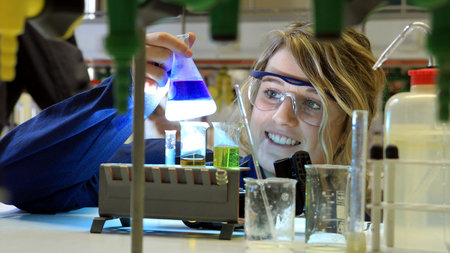 Schülerin experimentiert im Labor und hält einen mit einer blauen Substanz gefüllten Erlenmeyerkolben in der Hand