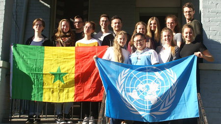 Mitglieder der Delegation halten UN-Flagge und Fahne von Senegal hoch.