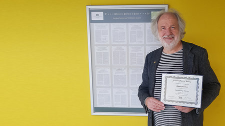 Olderly man with beard is holding a certificate.