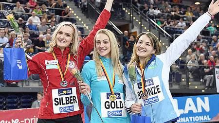 Drei jungen Frauen mit Medaillen und Blumen lachen.  