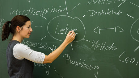 Junge Frau steht an einer Tafel und zeigt auf das Wort "Lehre".