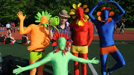 Fünf teilweise maskierte Männer in bunten Kostümen stehen auf dem Sportplatz