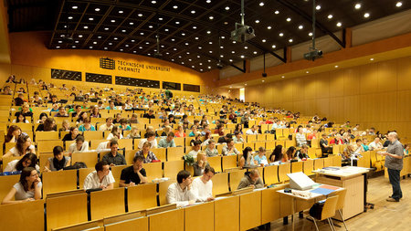 Viele Personen sitzen im Hörsaal, ein Mann referiert