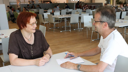 Mann und Frau sitzen an einem Tisch in der Mensa und sprechen miteinander.