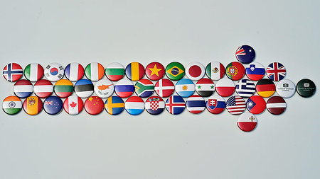 Viele Sticker von Flaggen unzähliger Länder liegen zu einem Pfeil arrangiert auf einem Tisch