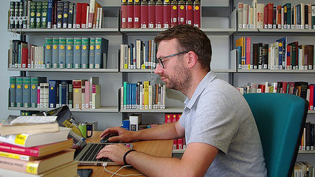 Junger Mann mit Brille sitzt vor einem Laptop.