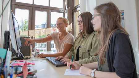 Drei Frauen sitzen vor einem Computermonitor