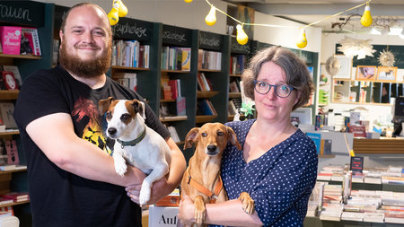 Mann und Frau stehen mit Hunden im Arm im Buchladen