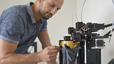 Ein junger Mann arbeitet an einem 3D-Drucker.