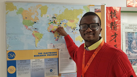 Junger Mann mit Brille zeigt auf einer Weltkarte auf Nigeria. 