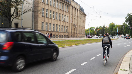 Radfahrerin fährt rechts neben einem Auto und schaut sich vor einem Spurwechsel nach links um