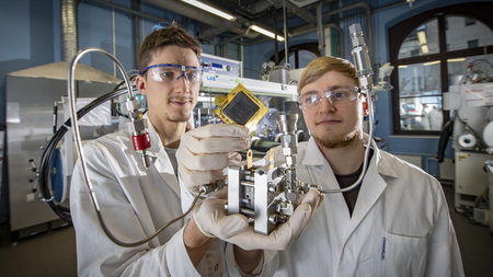 Zwei Männer halten im Chemielabor ein Bauteil hoch.