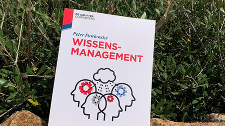 Ein Buch mit dem Titel Wissensmanagement liegt im Gras.