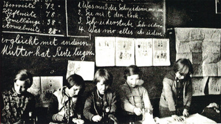 Fünf Kinder sitzen direkt vor einer vollgeschriebenen Tafel