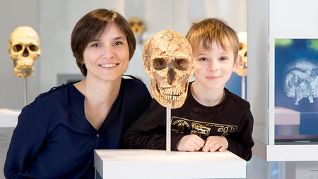 Eine Frau und ein Junge stehen neben einem Schädel eines Neandertalers.