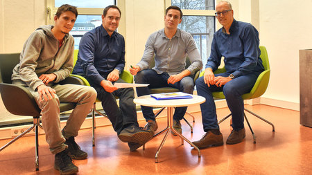 Vier Männer sitzen nebeneinander auf Stühlen.