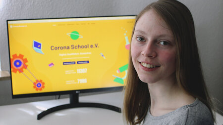 A young woman with long hair sits in front of a computer screen reading “Corona School e.V.”