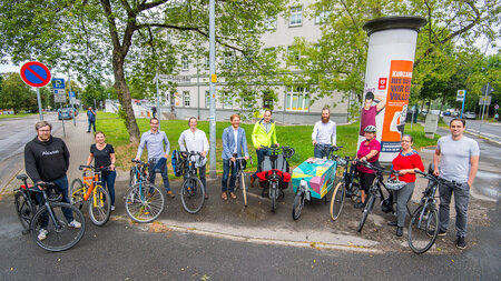 Zehn Personen stehen nebeneinander, jeder hält ein Fahrrad.