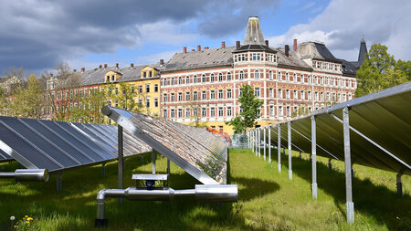 Sonnenkollektoren stehen auf einer Rasenfläche vor einer Häuserfront.