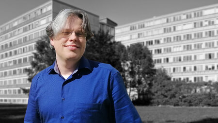 A man in the middle ages with middle long hair and glasses smiles.