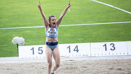 A woman in athletic gear celebrates next to a sand pit