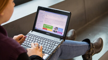 Eine junge Frau hat einen Laptop auf dem Schoß und recherchiert im Internet.
