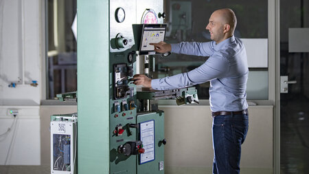 Mann bedient im Labor eine Maschine und berhrt dabei ein Display und ein Bedienfeld.