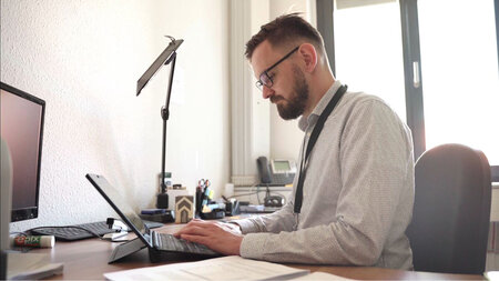 Photo of a man in glasses working at a laptop computer.