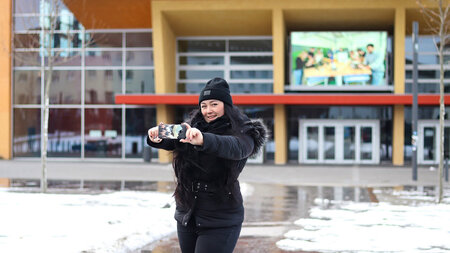 Junge Frau macht mit dem Handy ein Selfie vor einem Gebäude 
