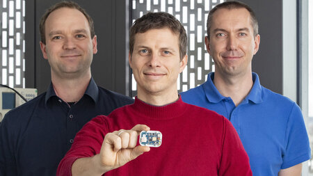 Three men. The man in the middle is holding a localizing chip.