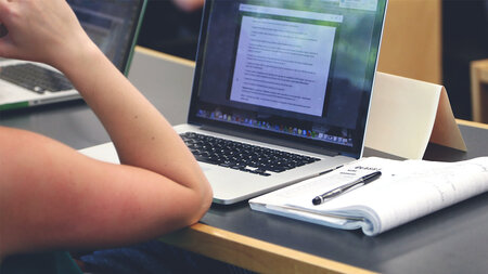 Frau sitzt an einem Tisch mit Laptop.