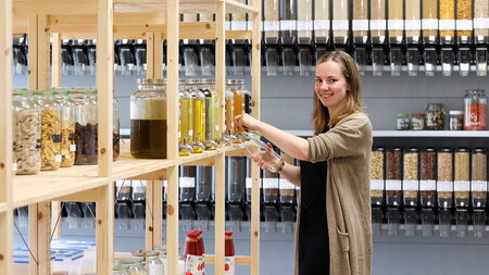 Frau steht vor einem Regal und füllt eine Flüssigkeit in eine Flasche.