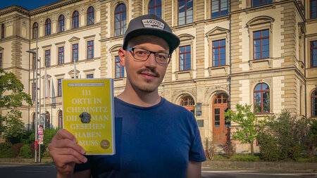Mann mit einem Buch in der Hand steht vor einem historischen Gebäude
