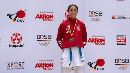 Eine jugn Frau im Karate-Anzug hat eine Medaille um den Hals und lacht. 