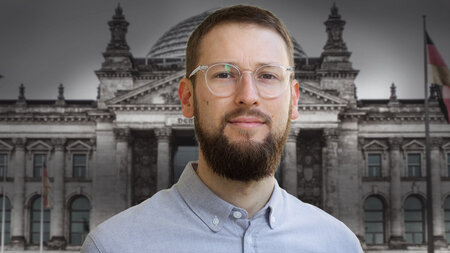 Ein junger Mann mit Brille steht vor dem Reichstagsgebäude.